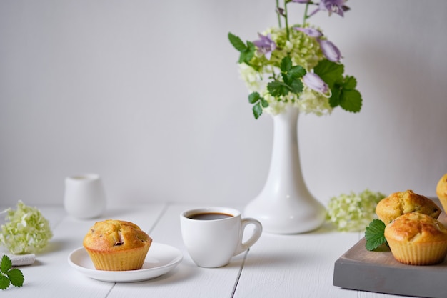 Coffee and fruit muffins with fresh peach for breakfast. Morning table with dessert, espresso and flowers in a vase on a white wooden table.