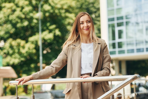 Coffee in hands Woman in formal wear standing outdoors in the city at daytime