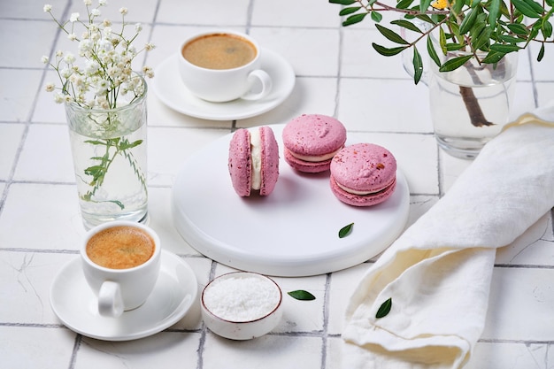 Coffee and macarons cakes for breakfast for two Morning table with dessert espresso and flowers in a vase on a white tiled table