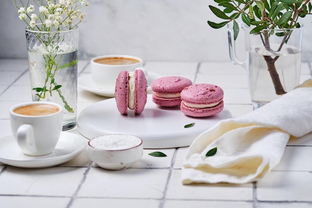 Coffee and macarons cakes for breakfast for two Morning table with dessert espresso and flowers in a vase on a white tiled table