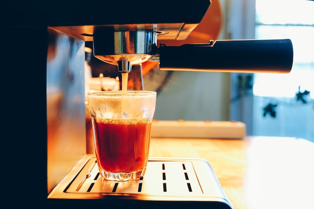 Coffee machine pours hot black tea in the glass.  