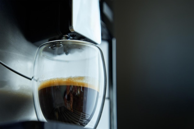 Photo coffee machine prepares fresh espresso in clear glass against dark background