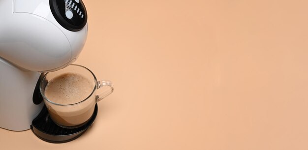 Coffee machine with cup of coffee on cream background