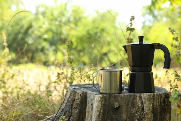 Coffee maker and metal cup on stump outdoor