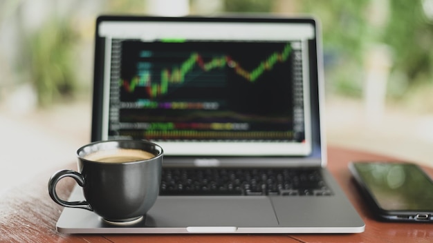 Coffee mug placed on laptop with stock graph on screen, Shot from the front.