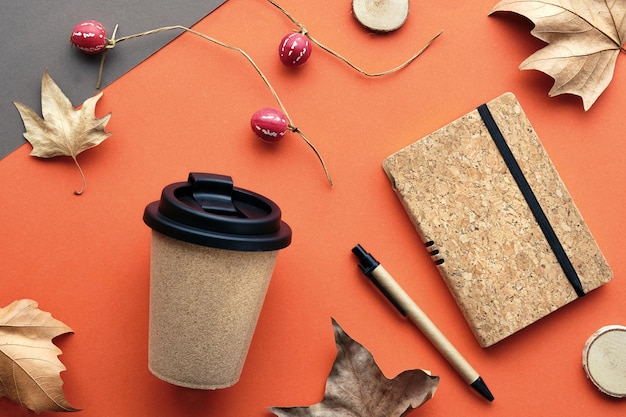 Coffee mug with natural cork band Coffee cup to go with dry sycamore leaves and deco pumpkins Notebook with matching cork cover Flat lay on orange grey paper Autumn backdrop