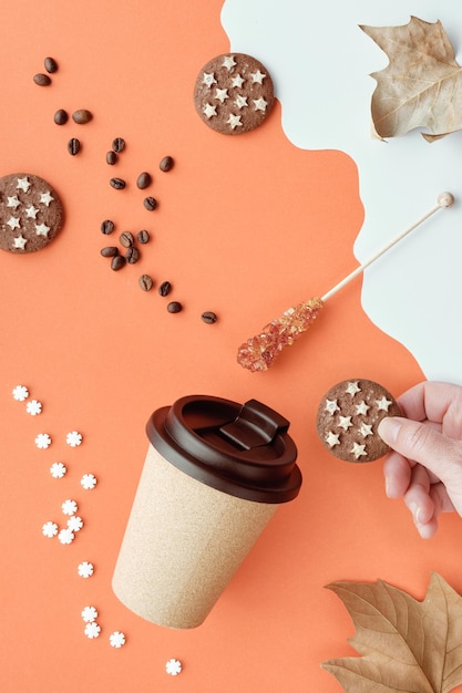 Coffee mug with natural cork Coffee cup to go on orange white Autumn background with dry leaves Coffee beans chocolate cookie in hand and sugar stick Wallpaper for social media stories