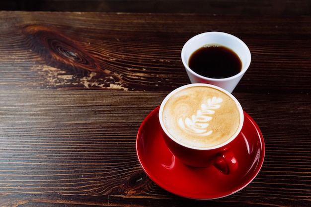 Coffee in a red cup with milk and latte art and coffee in a white cup on a table