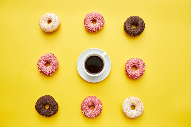 Coffee and sweet doughnuts knolling on yellow background cup of black coffee in center of treats