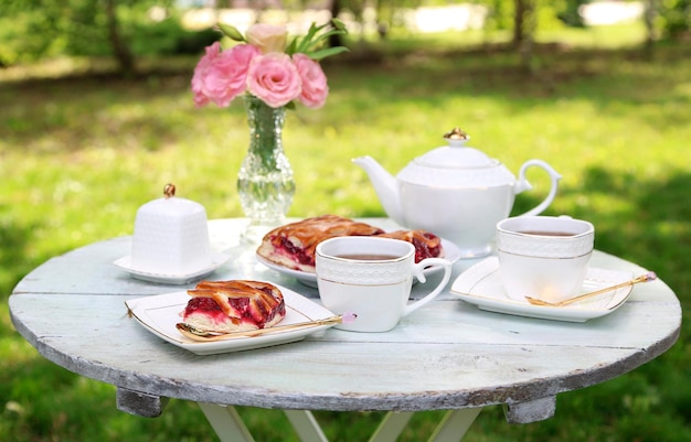 Coffee table with teacups and tasty pie in garden