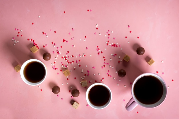 Coffee tea cups, sweets candy chocolate on pink hearts background. Valentines day 14 february minimal concept. Flat lay, above, top view