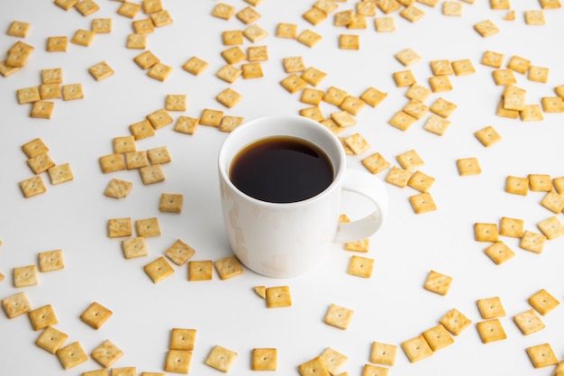 Coffee in a white cup on the background of a scattered crispy cracker on a white background