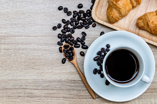 Coffee in white cup with coffee bean and croissants on wooden table, Breakfast concept