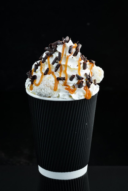 Coffee with caramel and cream in a paper cup on a black background Free space for text