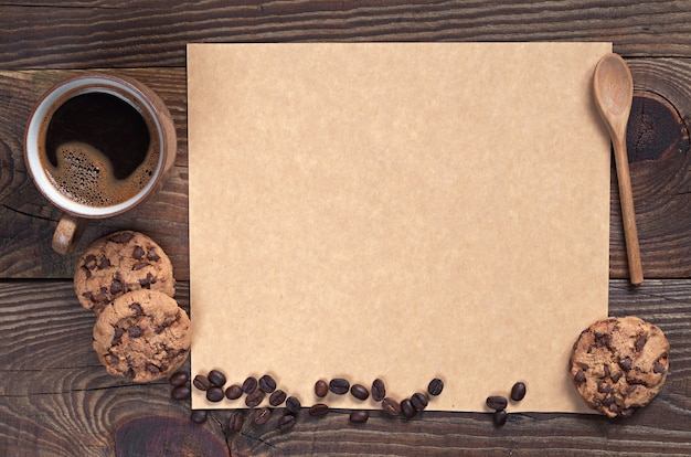 Coffee with chocolate cookies and empty brown paper for text on dark wooden background, top view