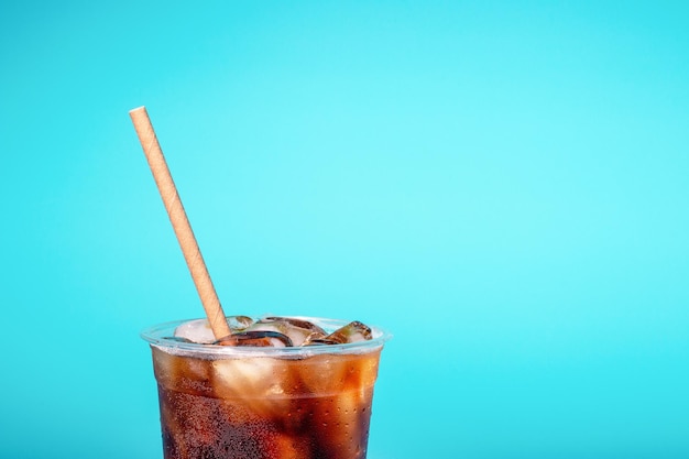 Coffee with ice in a plastic glass with a tube on blue background a copy of the space