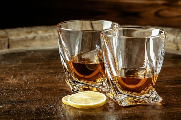 Cognac in glasses with lemon pieces over wooden table