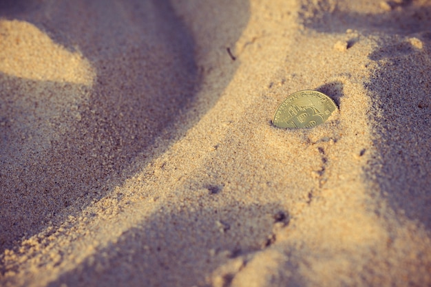 Coin bitcoin buried in the sand on the beach