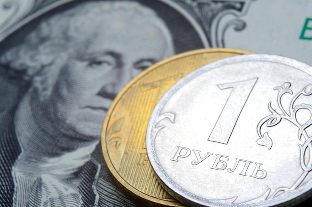 A coin with a face value of 1 ruble lies on a banknote of the American dollar closeup