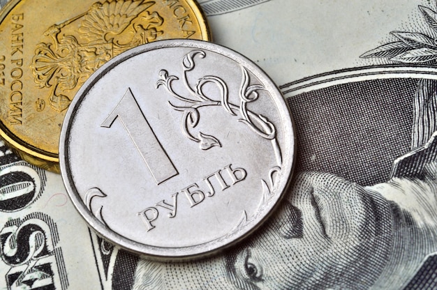 A coin with a face value of 1 ruble lies on a banknote of the American dollar closeup