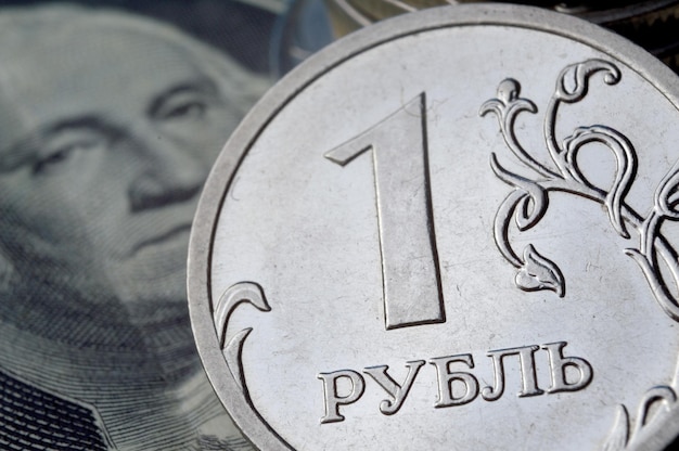 A coin with a face value of 1 ruble lies on a banknote of the American dollar closeup