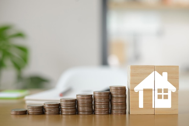 Coins are laid out on a wooden table and wooden blocks in the shape of a house Demonstrates saving money to buy a house