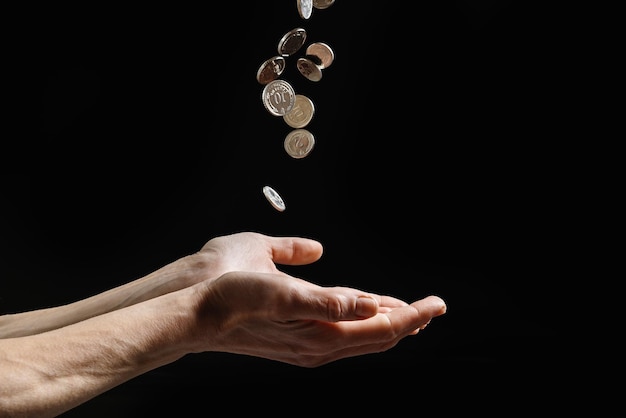 Coins fall into the hands of a poor man financial aid on dark background whit copy space