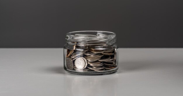 Coins in glass jar currency money on dark gray background for business and finance concept copy space Jar full of coins Business finance saving money or investment concept