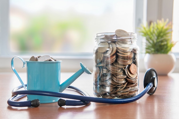 Coins in a glass jar. Watering and stethoscope. Health insurance. Investment concept. Accumulation of capital.