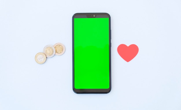 Coins and heart near smartphone with blank copy space on screen isolated on white