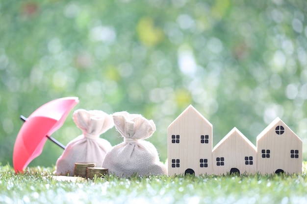 Coins money in the bag under the umbrella and model house on natural green background