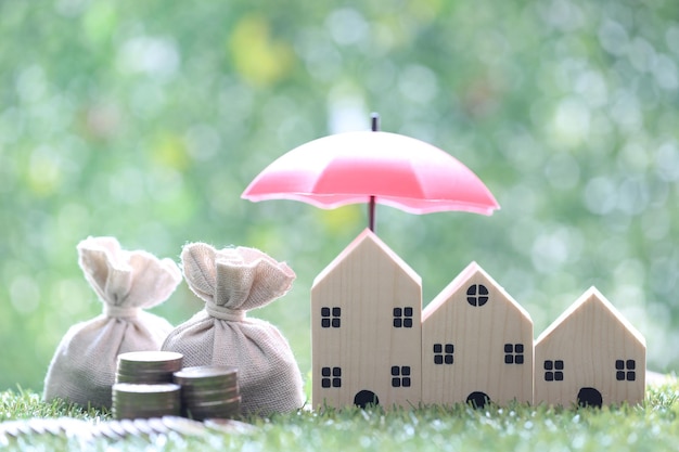 Coins money in the bag under the umbrella and model house on natural green background