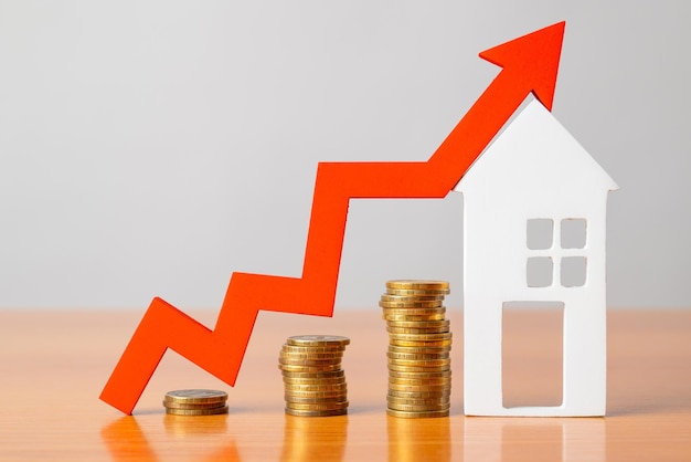 Coins on a table a red up arrow and house The concept of the rising price of real estate