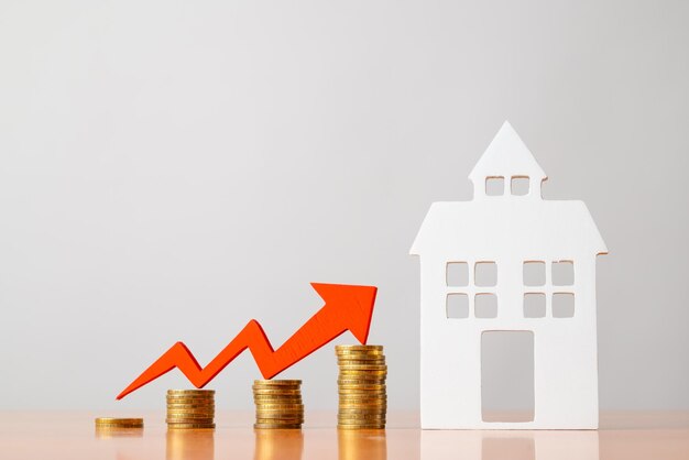 Coins on a table a red up arrow and house The concept of the rising price of real estate