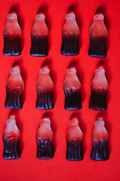 Cola jelly gummy candies in four rows at red background