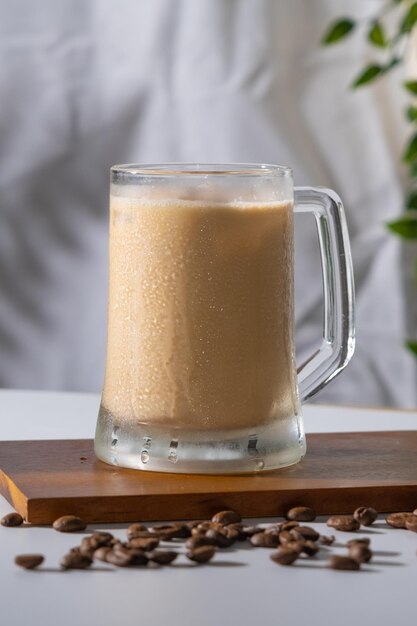 Cold coffee drink glass with ice and cream milk on old white table in abstract silhouette shadow white background of natural leaves tree branch falling on wall latte and cappuccino refreshment