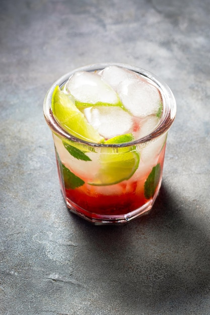 Cold detox water with lime strawberry mint in the glass with ice cubes on gray background close up