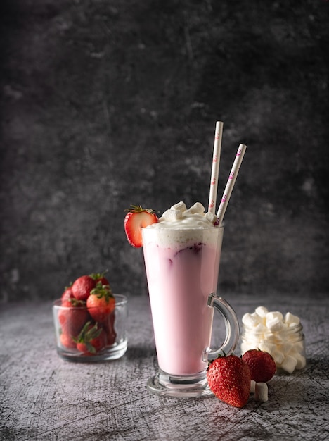 A cold drink milk strawberry milkshake with fresh strawberries and cream in a high transparent glass