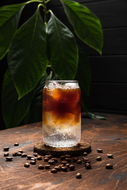 Cold espresso tonic A highball glass filled with ice cubes tonic soda water coffee beans around wooden background