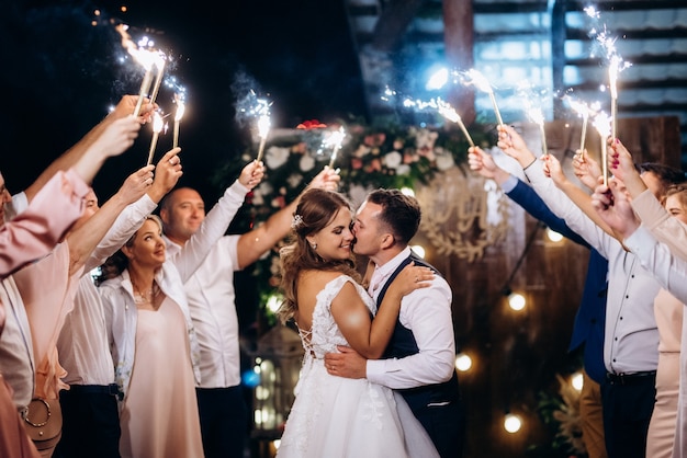 Cold fire from cake candles and fireworks in the hands of people around the newlyweds