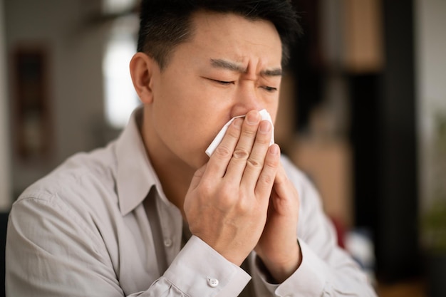 Cold flu allergy concept sick middle aged asian man sneezing in napkin ill male feeling unwell