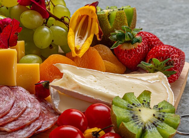 Cold and fruit board served on wood and marble background with cheese ham brown salami strawberries ...