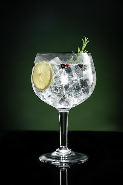 Cold glass of gin tonic with ice on dark green background with copy space Vertical format