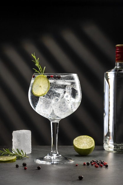 Cold glass of gin tonic with ice and hard shadows on dark gray background with copy space Vertical format