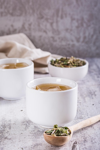 Cold green Japanese hojicha tea with ice in cups and dry tea in a bowl on the table Vertical view