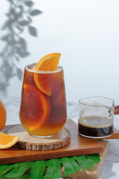 Cold Iced black coffee mixed with orange juice and orange slices in glass on wooden plate