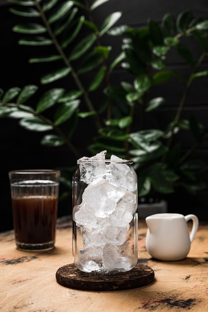 Cold iced latte coffee in the making A tall highball glass filled with ice cubes a milk jug espresso in the glass