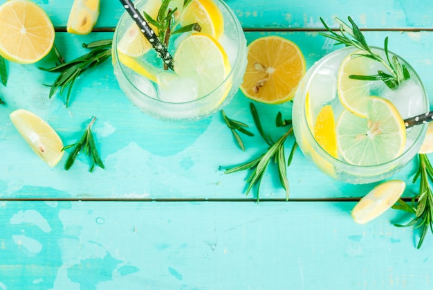 Cold lemonade or alcohol vodka cocktail with lemon and rosemary, on light blue table,  top view