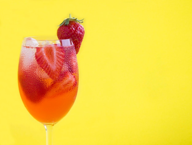 Cold lemonade or infused water strawberry in the wine glass on the yellow background Copy space Closeup