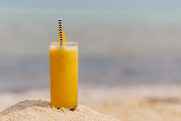 Cold multi fruit cocktail drink with slices of mango on beach background